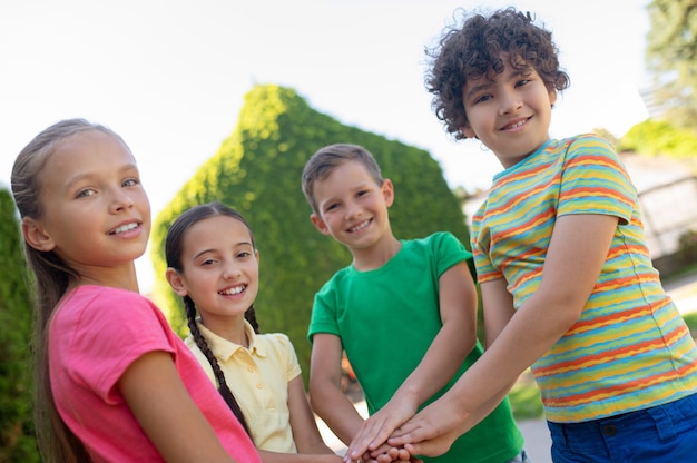 Freunde. fröhliche fröhliche schulkinder in hellen kleidern, die händchen halten als zeichen einer starken freundschaft, die an einem schönen tag im park stehen