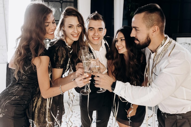 Freunde in stilvoller, eleganter Kleidung lächeln zusammen und halten Gläser Champagner in den Händen