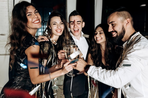 Freunde in stilvoller, eleganter Kleidung lächeln zusammen und halten Gläser Champagner in den Händen