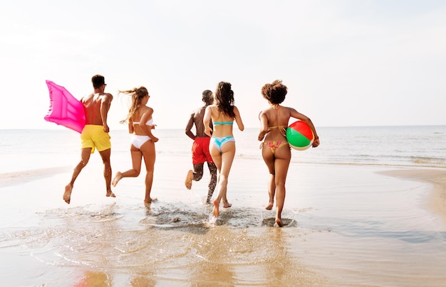 Freunde laufen mit Strandball und Schwimmmatratze