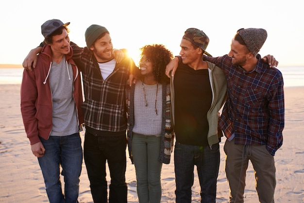 Freunde machen die Welt zu einem besseren Ort Aufnahme einer Gruppe von Freunden, die bei Sonnenuntergang am Strand spazieren gehen