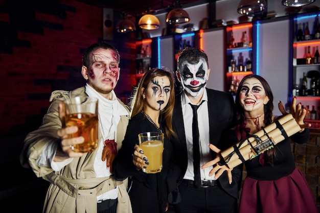 Freunde mit Bombe in den Händen sind auf der thematischen Halloween-Party in gruseligem Make-up und Kostümen.