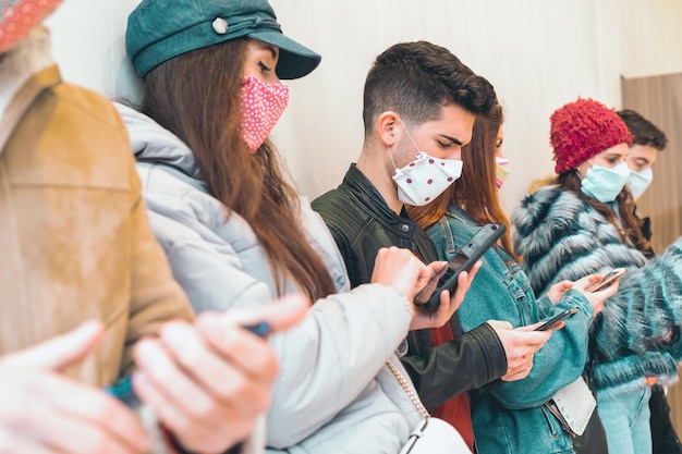 Freunde mit Gesichtsmasken, die sich Inhalte auf Smartphones ansehen, die zusammenstehen Neues normales Konzept junger Menschen, die süchtig nach Mobiltelefonen, Internet und sozialen Medien sind