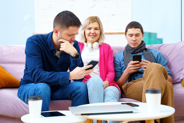 Freunde sitzen auf der Couch und unterhalten sich mit einem Smartphone-Desktop-Computer-Laptop