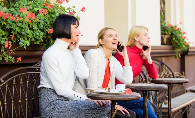 Freunde sitzen im Café und unterhalten sich gerne. Besessen vom Sprechen. Verwenden digitaler Geräte. Gruppe von Frauen auf der Caféterrasse. Freundschaftstreffen