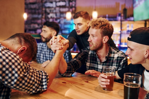 Freunde spielen Armdrücken Gruppe von Menschen zusammen drinnen in der Kneipe haben Spaß am Wochenende