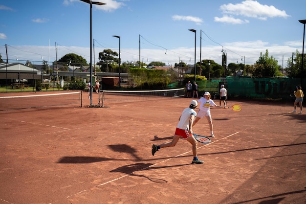 Freunde spielen Tennis auf einem Lehmplatz, bewässern und versacken einen Lehmplatz und betreiben die Wartung eines Tennisplatzes.