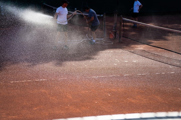 Freunde spielen Tennis auf einem Lehmplatz, bewässern und versacken einen Lehmplatz und betreiben die Wartung eines Tennisplatzes.
