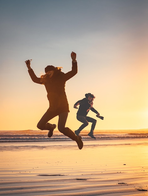 Freunde springen bei Sonnenuntergang am Strand vor klarem Himmel