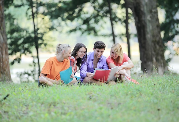 Freunde von Studenten lesen Bücher, die auf dem Rasen im Park sitzen