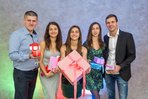 Freundesgesellschaft, die Neujahr feiert. Frauen und Männer, die bunte Geschenkboxen auf abstraktem Hintergrund halten