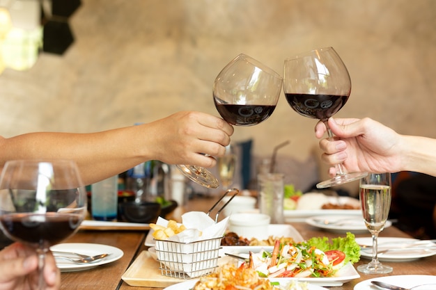 Freundfeiermittagessen mit den Händen, die Glasrotwein mit Lebensmittel rösten.