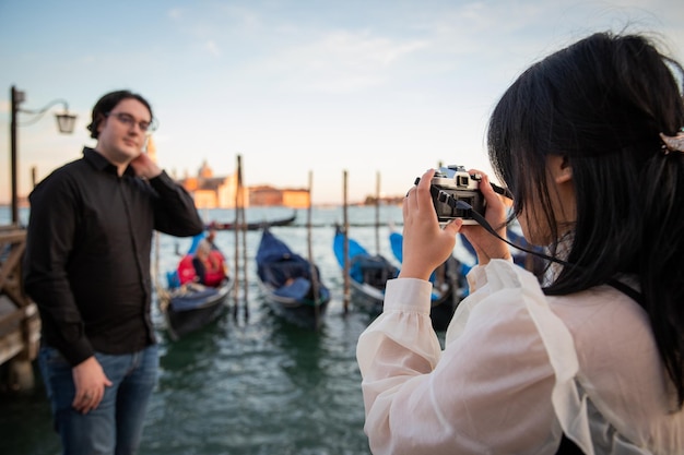 Freundin macht ein Foto von ihrem Freund, während sie im Urlaub in Venedig sind, Touristen, die die Stadt der Liebe besuchen