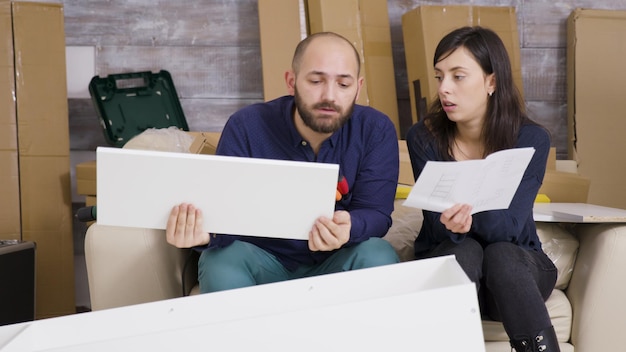 Freundin und Freund bauen in ihrer neuen Wohnung Möbel zusammen und lesen Anleitungen.