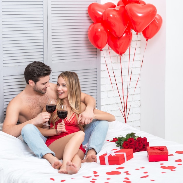 Freundin und Freund trinken Rotwein im Bett am Valentinstag