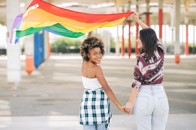 Freundinnen halten Händchen beim Gehen mit einer LGBT-Flagge