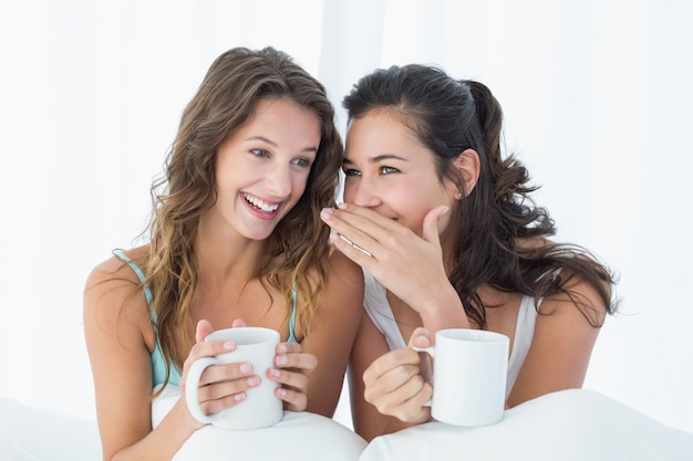 Freundinnen mit Kaffeetassen, die im Bett klatschen