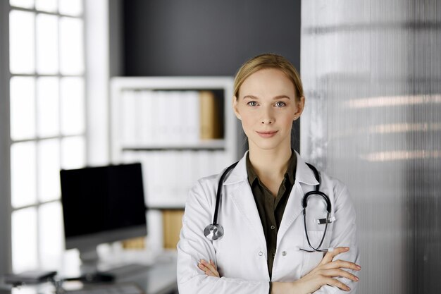 Foto freundlich lächelnde ärztin, die in der klinik steht. porträt einer freundlichen ärztin. perfekte medizinische versorgung im krankenhaus.