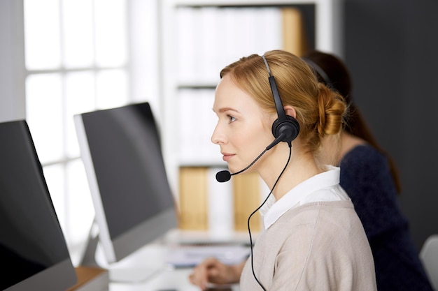 Freundliche Geschäftsfrau, die per Headset spricht, während sie im Büro sitzt. Call Center und diverse Personengruppen in der Wirtschaft.