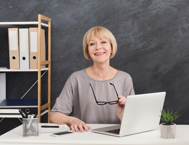 Freundliche Sekretärin mit Brille, die im Büro an Laptop arbeitet