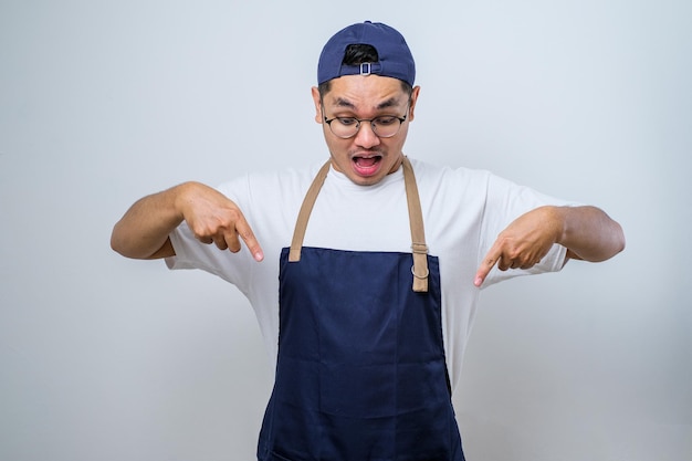 Foto freundlicher, fröhlicher asiatischer barista mit schürze, der mit dem finger nach unten zeigt und lächelt, als er werbung mit ankündigung zeigt