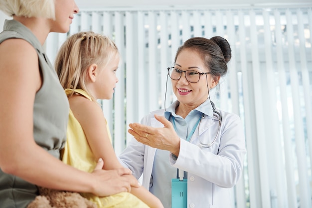 Freundlicher Kinderarzt, der mit kleinem Mädchen spricht