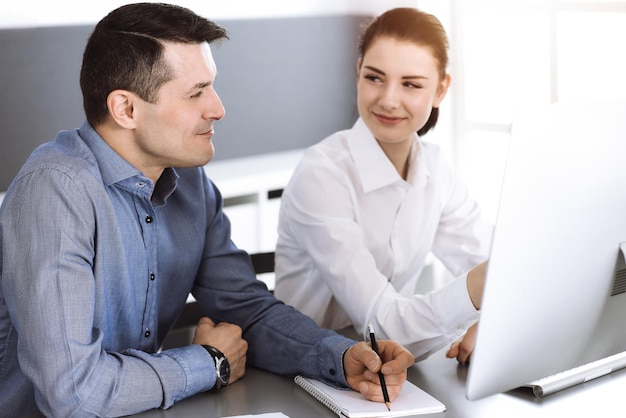 Freundlicher lächelnder Geschäftsmann und Frau, die mit Computer im modernen Büro arbeiten. Kopfschuss bei Besprechung oder am Arbeitsplatz. Teamwork, Partnerschaft und Geschäftskonzept.