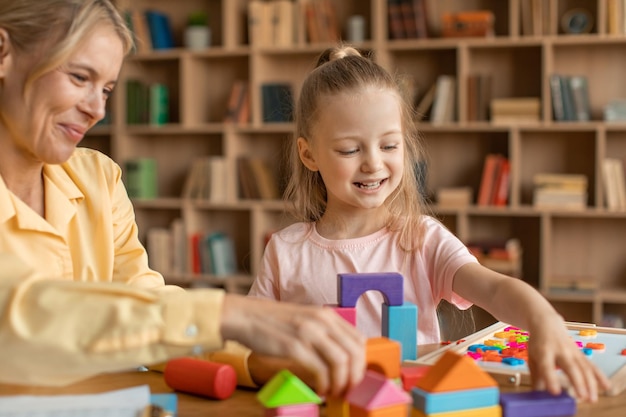 Freundlicher Spezialist für Kinderentwicklung beobachtet Mädchen im Vorschulalter kleines Kind, das Pyramiden aus bunten Holzblöcken macht