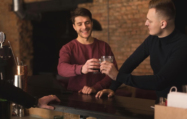 Foto freundliches gespräch in der bar. draufsicht auf zwei glückliche junge männer, die miteinander reden und whisky genießen, an der bartheke jubeln, platz kopieren