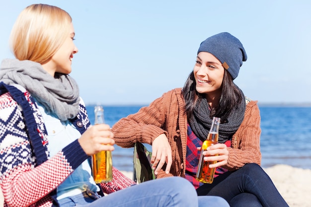 Freundliches Gespräch. Zwei schöne junge Frauen trinken Bier und reden miteinander, während sie zusammen am Strand sitzen