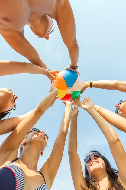 Freundschaft, Glück, Sommerferien, Feiertage und Personenkonzept - Gruppe lächelnder Freunde in Badebekleidung, die im Kreis mit Wasserball über blauem Himmel stehen