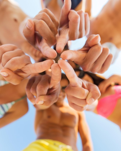 Freundschaft, Glück, Sommerferien, Feiertage und Personenkonzept - Nahaufnahme lächelnder Freunde in Badebekleidung, die im Kreis über blauem Himmel stehen