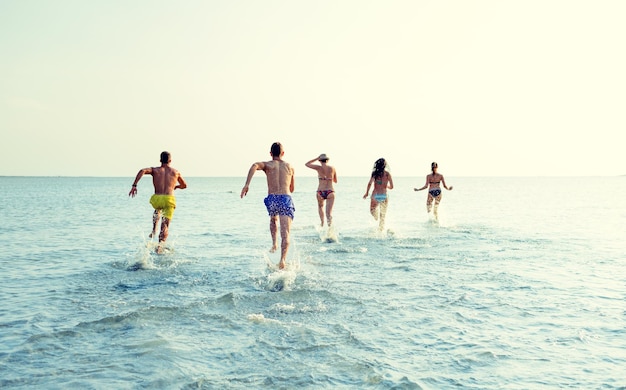 freundschaft, meer, sommerferien, ferien und personenkonzept - gruppe lächelnder freunde in badebekleidung, die von hinten am strand laufen