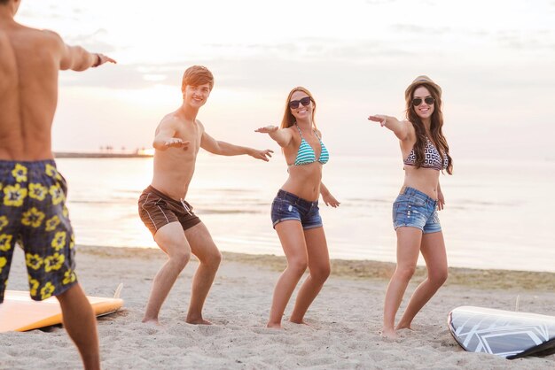 freundschaft, meer, sommerferien, wassersport und menschenkonzept - gruppe lächelnder freunde, die badebekleidung und sonnenbrille mit surfbrettern am strand tragen