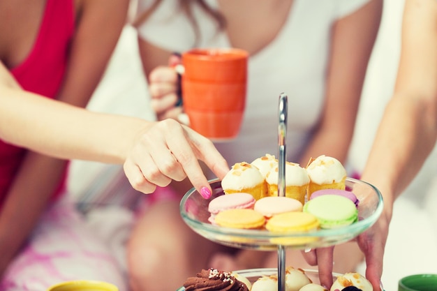 Freundschaft, Menschen, Pyjama-Party und Junk-Food-Konzept - Nahaufnahme von Freunden oder Mädchen im Teenageralter, die zu Hause Süßigkeiten vom Kuchenstand essen