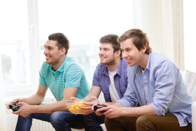 Foto freundschaft, technologie, spiele und heimkonzept - lächelnde männliche freunde, die zu hause videospiele spielen