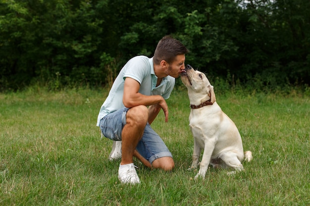 Freundschaft und Liebe von Mensch und Hund. Glücklicher junger Mann, der mit seinem Freund - Hund Labrador küsst