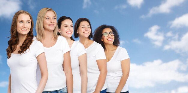 freundschaft, vielfältig, körperpositiv und personenkonzept - gruppe glücklicher frauen unterschiedlicher größe in weißen t-shirts über blauem himmel und wolkenhintergrund