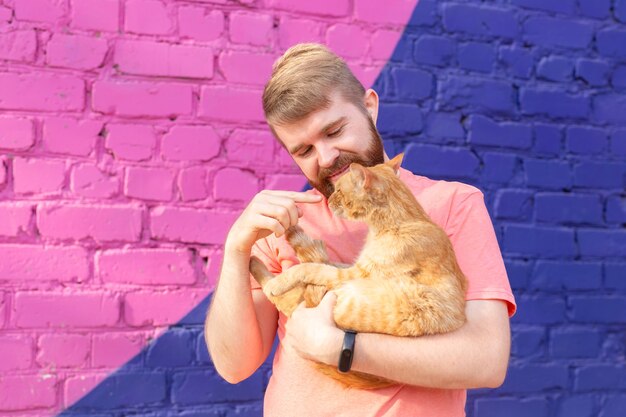 Freundschaft zwischen Mann und Katze auf dem Hintergrund der bunten Wand im Freien.