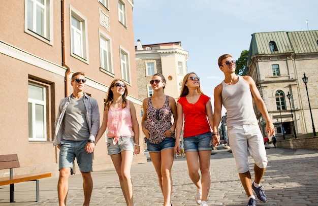 Freundschafts-, Freizeit-, Sommer-, Gestik- und Personenkonzept - Gruppe lächelnder Freunde, die in der Stadt spazieren gehen und Händchen halten