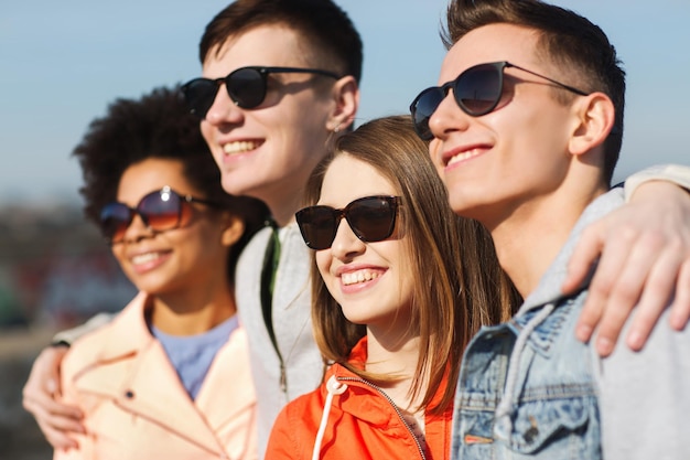 Freundschafts-, Tourismus-, Reise- und Personenkonzept - Gruppe glücklicher Teenager-Freunde mit Sonnenbrille, die sich im Freien umarmen