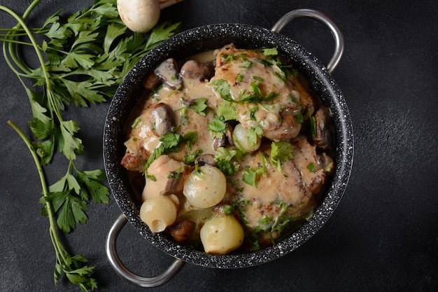 Fricassé - Cozinha Francesa. Frango estufado em molho cremoso com cogumelos em uma caçarola sobre uma mesa preta