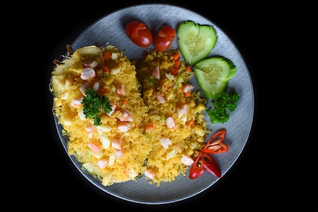 Fride arroz con mariscos en una piña con verduras en plato azul aislado sobre fondo negro para