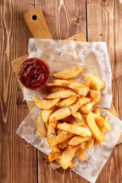 Fried Potatoes na tábua de madeira velha com ketchup de tigela.