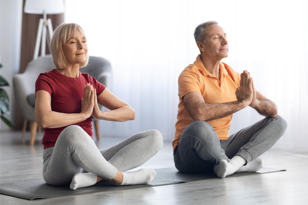 Friedliche Rentner sitzen auf Fitnessmatte in Lotus-Pose