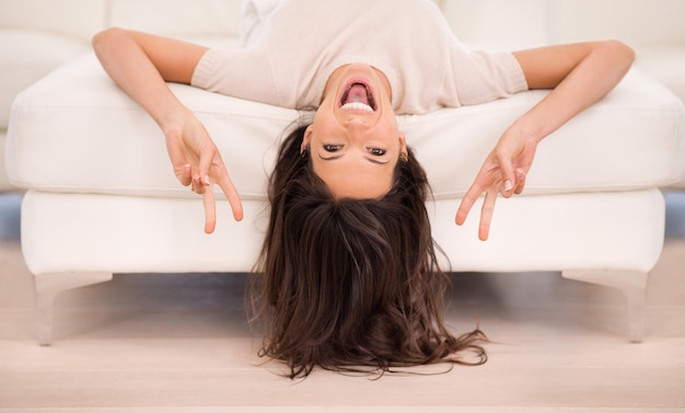 Friedliche Zeit in der Lounge Eine schöne Frau, die das Peace-Zeichen macht, während sie verkehrt herum auf einer Couch liegt