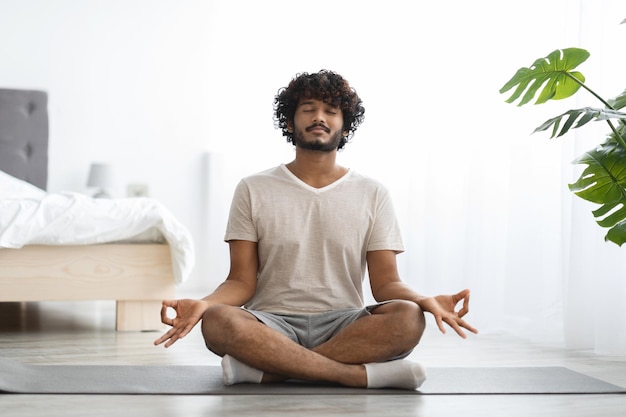 Friedlicher indischer Mann, der zu Hause Yoga praktiziert und meditiert