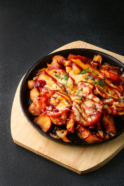 Frigideira com batata, carne e tomate em fundo de concreto preto