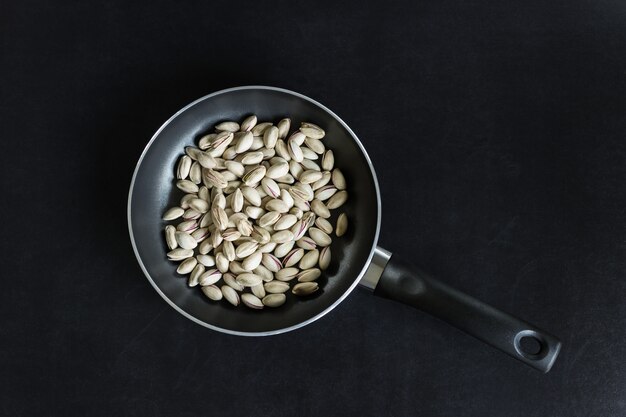 Frigideira com pistachios em um fundo preto.