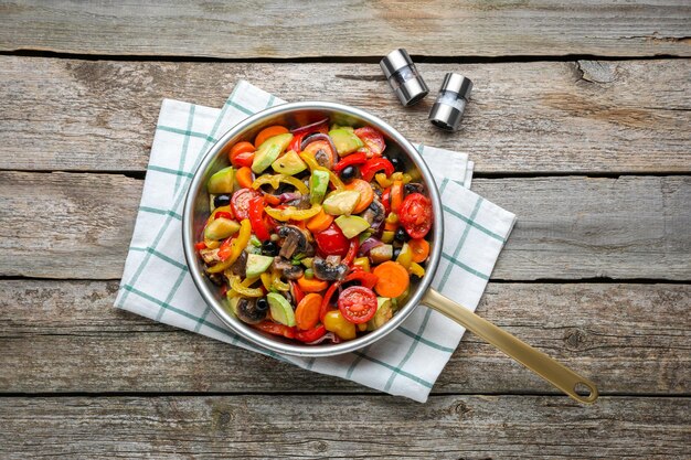 Foto frigideira com saborosos legumes cozidos e cogumelos na mesa de madeira plana